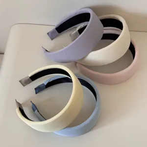 Macro view of multiple wide padded headbands featuring soft ribbed fabric in various pastel colors