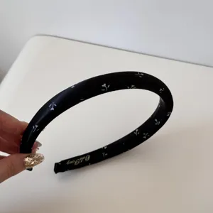 Détail d'un serre-tête en satin noir orné de petits motifs floraux blancs et logo