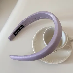 Detalle de una diadema de satén lavanda acolchada con una etiqueta tejida 'HANDMADE'