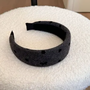 Détail rapproché d'un serre-tête en peluche gris foncé à pois noirs avec un petit nœud