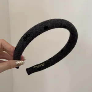 Close-up shot of a wide dark grey woolly headband featuring elegant black heart patterns.