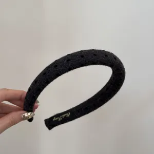 Close-up of a wide dark grey padded headband with subtle polka dot texture and brand label.