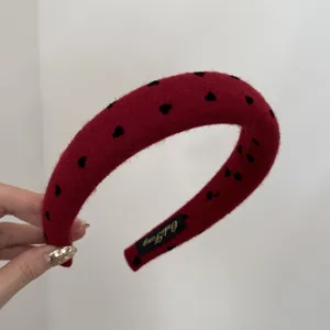Close-up of a red wide headband featuring black heart patterns and soft fabric texture