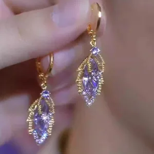 Gros plan de boucles d'oreilles feuille d'or avec des cristaux violets étincelants