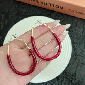 Close-up detail of red enamel and gold geometric oval hoop earrings held in hand