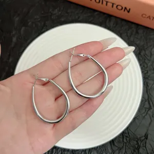 Detailed macro view of stylish silver geometric teardrop hoop earrings held in hand