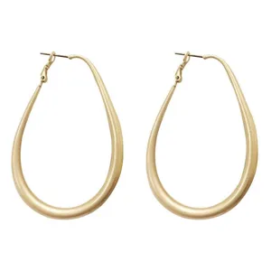 Detail view of large gold oval hoop earrings showing the smooth matte metal finish