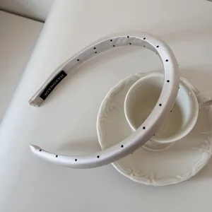 Détail d'un serre-tête ivoire à pois avec étiquette fait main sur une tasse blanche