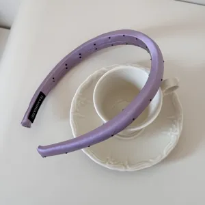 Gros plan détaillé d'un serre-tête en satin violet à pois sur une tasse à thé blanche.