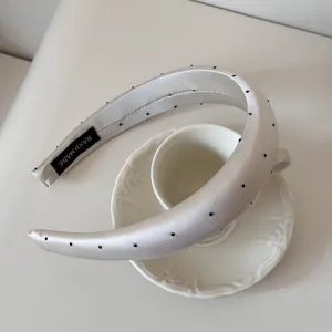 Détail d'un serre-tête élégant en satin à pois posé sur une tasse à café blanche