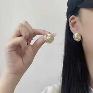 Detailed close-up showing textured gold circular earrings with elegant white pearl on model