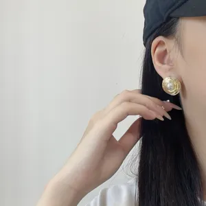 Detail view of elegant irregular gold stud earrings with a pearl center on model's ear
