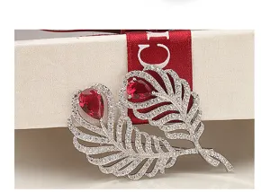Detail view of luxury feather brooch with red pear-cut zircon and white crystals.