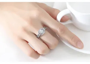 Primer plano de un elegante anillo halo de cristal plateado en mano junto a una taza blanca