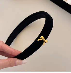 Close-up detail of a black velvet headband featuring a delicate gold bow charm accessory.