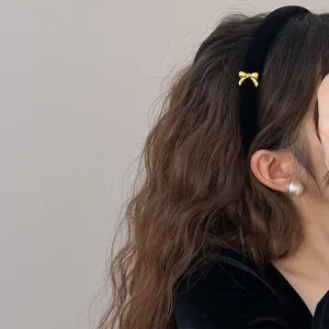 Detail view of a black velvet headband with a dainty gold bow on wavy brown hair