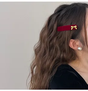 Detail view of a burgundy velvet hair clip with a stylish golden bow on wavy hair.