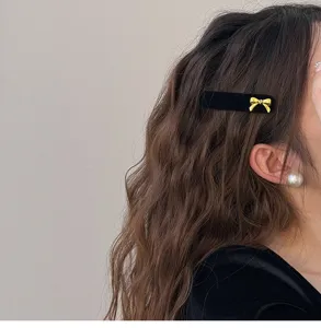 Close-up detail of black velvet hair clip with a delicate gold bow accessory for women