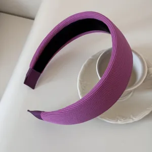 Close-up of a wide purple ribbed padded headband placed on a white ceramic saucer.