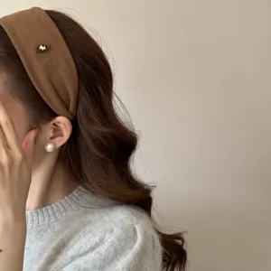 Détail d'un bandeau large en daim marron avec un petit emblème de cheval métallique