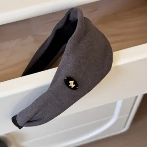Détail d'un serre-tête rembourré gris orné d'une petite breloque de cheval dorée sur du feutre