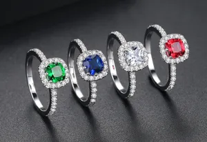 Primer plano de cuatro elegantes anillos halo con gemas de color verde, azul, blanco y rojo