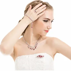 Elegante conjunto de joyas de boda con circonitas rojas en forma de gota y vestido blanco.