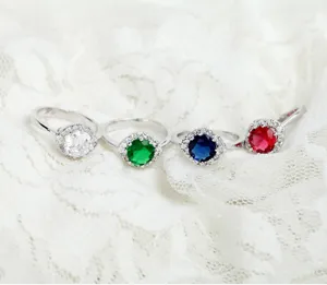 Close-up van vier luxe messing ringen met kleurrijke zirkoniasteentjes op witte kant.