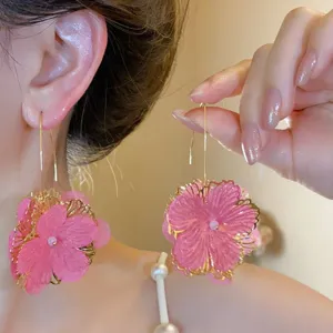 Dettaglio dei grandi orecchini a fiore in rete rosa con bordi metallici dorati.