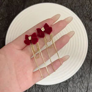 Dettaglio macro di eleganti orecchini a fiocco rosso con lunghe nappe a catena dorata.
