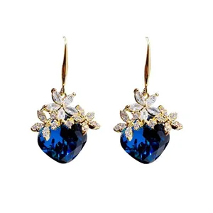 Dettaglio di eleganti orecchini a fiore dorati con pendenti in cristallo a cuore blu.
