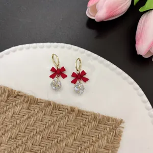 Detailansicht von koreanischen Goldohrringen mit roter Schleife und glänzendem Zirkonia-Ball.