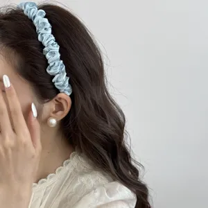 Close-up detail showing the elegant pleated texture of a light blue satin headband on hair