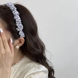 Detail view of a silver pleated satin headband worn by an Asian model with pearl earring