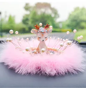 Close-up of a cute deer car ornament with pink feathers and pearls on a dashboard