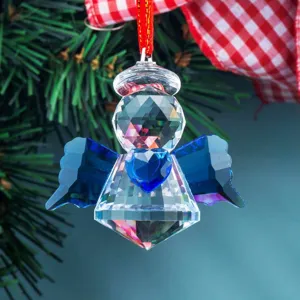 Close-up of faceted crystal angel ornament with blue heart and wings hanging on tree