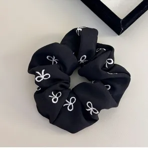 Vista dettagliata di uno scrunchie in tessuto nero con motivi a fiocco ricamati bianchi