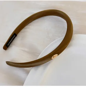 Gros plan d'un serre-tête en satin vert olive avec emblème doré et rembourrage en éponge