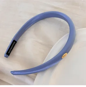 Vue détaillée d'un serre-tête en satin bleu avec une étiquette dorée ovale chic.