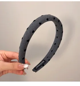 Détail d'un serre-tête rembourré gris avec motif de cœurs noirs et étiquette faite main.