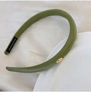Gros plan d'un serre-tête en satin vert olive avec un élégant médaillon doré chic