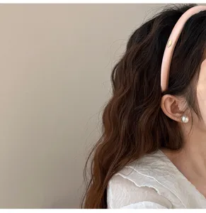 Vue détaillée d'un serre-tête en satin rose avec emblème doré sur cheveux bruns ondulés
