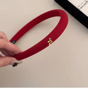 Primer plano de diadema roja acolchada con un delicado detalle de lazo dorado.