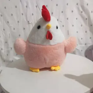 Soft plush chicken toy doll in pink and white color shown sitting on a white table.