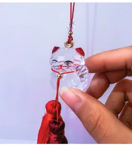 Detail view of a faceted clear crystal lucky cat hanging ornament with vibrant red tassels