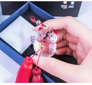 Close-up of faceted crystal Maneki Neko charm with red tassels and gold ring