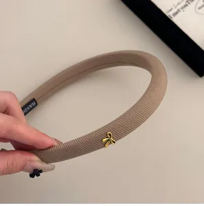 Primer plano detallado de una diadema de tela de esponja marrón con un pequeño lazo dorado