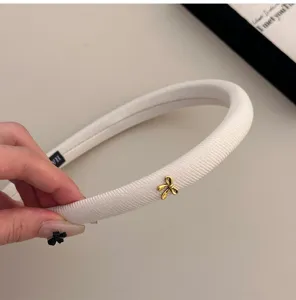 Detalle del pequeño lazo dorado en una diadema acolchada blanca minimalista de esponja