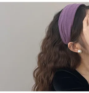 Gros plan d'un bandeau large en tricot violet sur des cheveux bruns ondulés soyeux