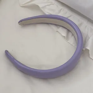 Detailed shot of a purple padded leather headband on white ruffled fabric.